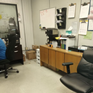 A man seated at a desk in an office, focused on his work with a computer and paperwork around him.