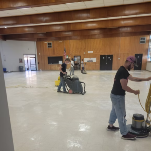 Two men vacuuming a spacious room, focused on cleaning the floor and maintaining a tidy environment.