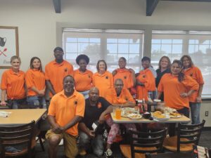 A group of individuals wearing orange shirts smiles and poses together for a group photo.