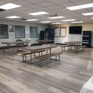 A spacious room featuring multiple tables and benches arranged for group activities or gatherings.